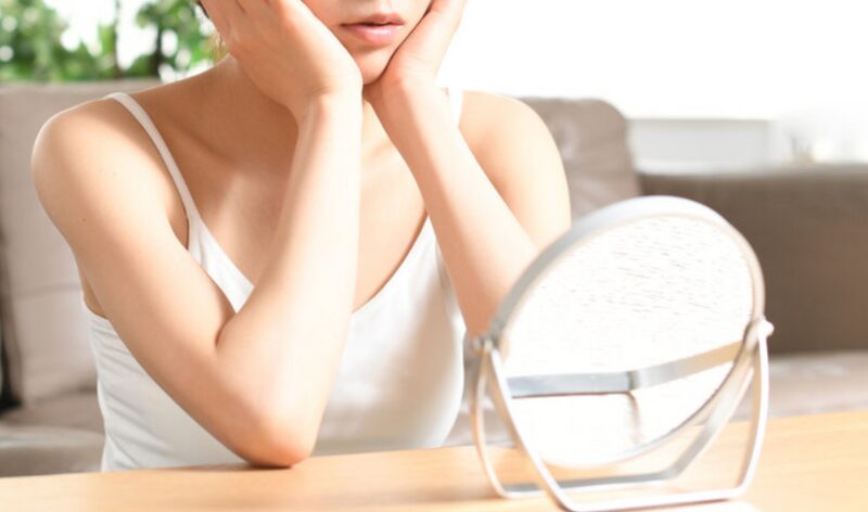 鏡を見ながら頬に手を当てて、肌の調子を気にする女性のアップ