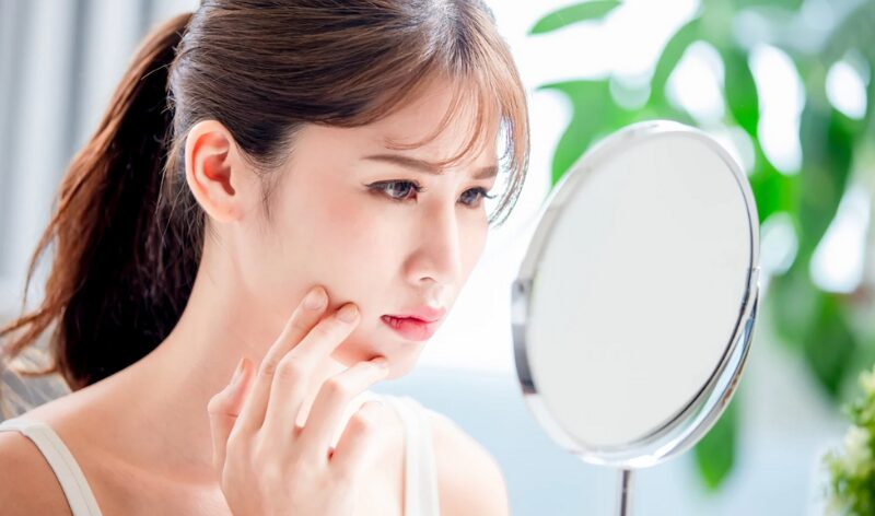 鏡を見て、肌のベタつきに悩んでいる女性