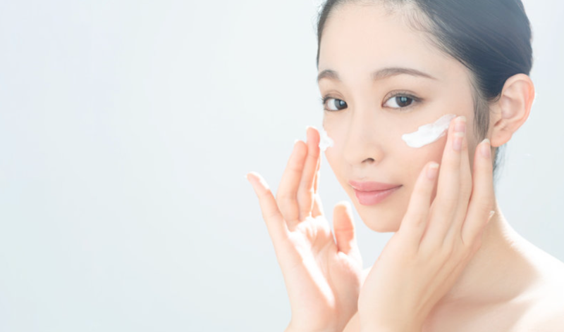 顔にクリームを塗る女性。保湿ケアを丁寧に行いながら、肌の明るさを保つスキンケアの様子。