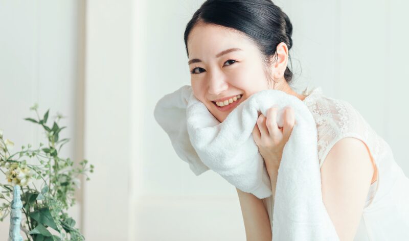 朝の洗顔後、タオルでやさしく顔を拭く女性。清潔で明るい印象の肌を保つシンプルケアのイメージ。