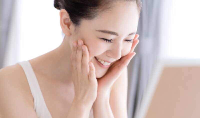 スキンケア中に両手で頬を包み込み、うれしそうに笑顔を見せる女性。