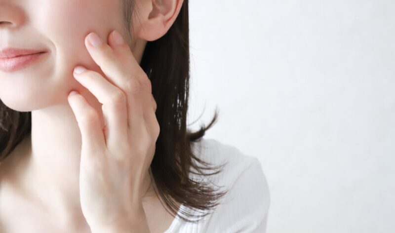頬に触れながら肌の調子を確認する女性。スキンケア後の肌のくすみや赤みを気にしている様子。